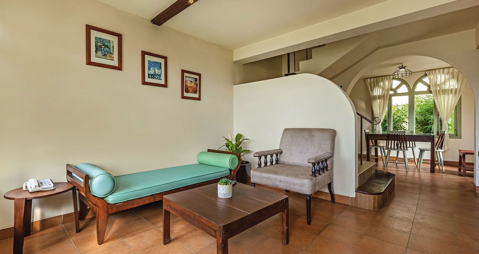 Living area at Mango Hill Shola, Ooty, with cushioned seating, a coffee table, and arched windows allowing in natural light.