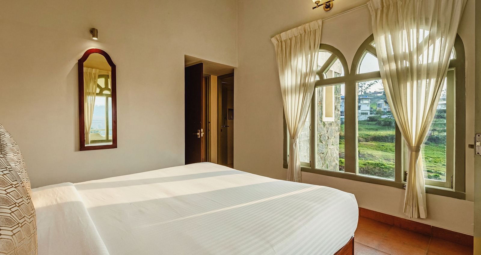 Bedroom at Mango Hill Shola, Ooty, featuring a double bed and large curtained windows allowing natural light into the room.