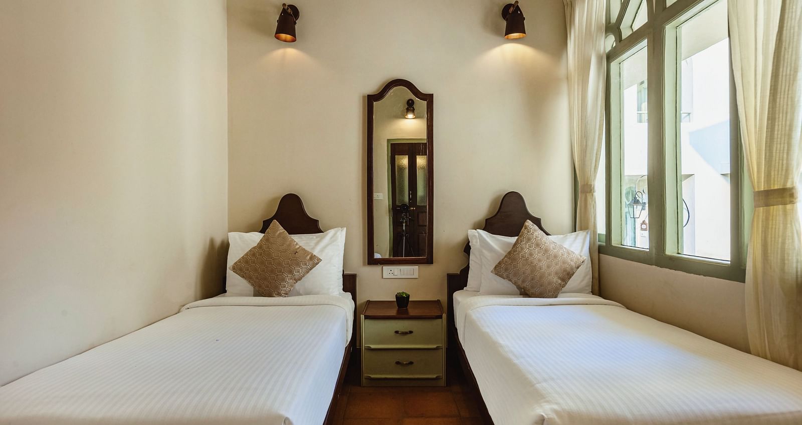 Twin bedroom at Mango Hill Shola, Ooty, with two single beds, bedside lamps, and windows providing daylight.