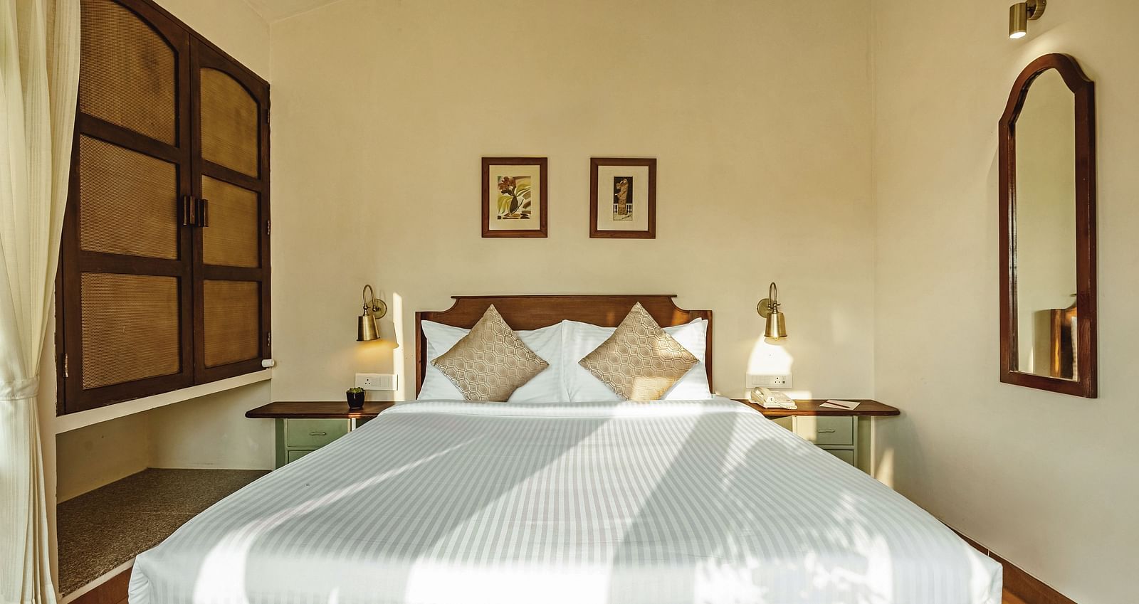 Bedroom at Mango Hill Shola, Ooty, with a double bed, striped bedding, bedside tables, and framed pictures on the wall.