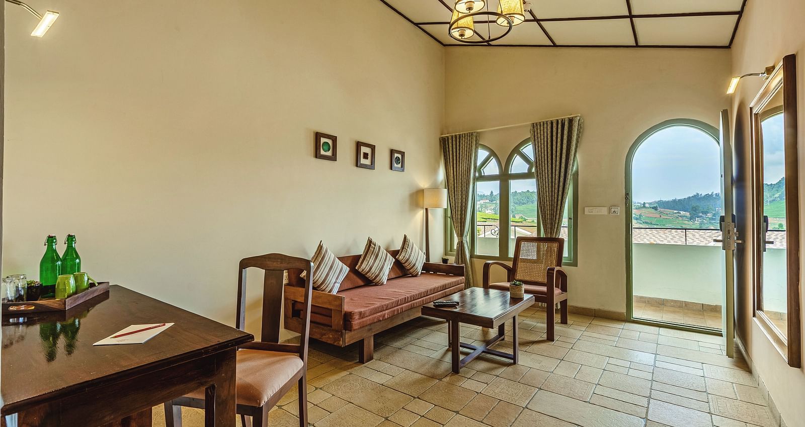 Bright room at Mango Hill Shola, Ooty with a writing desk, refreshments, and large arched doors opening to scenic views.