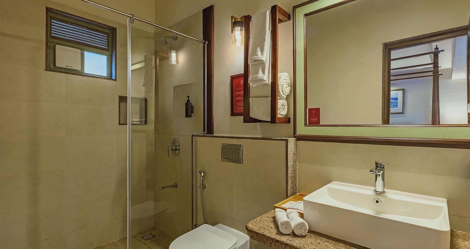 Contemporary bathroom at Mango Hill Shola, Ooty showcasing a wide mirror, clean countertop, and walk-in glass shower.