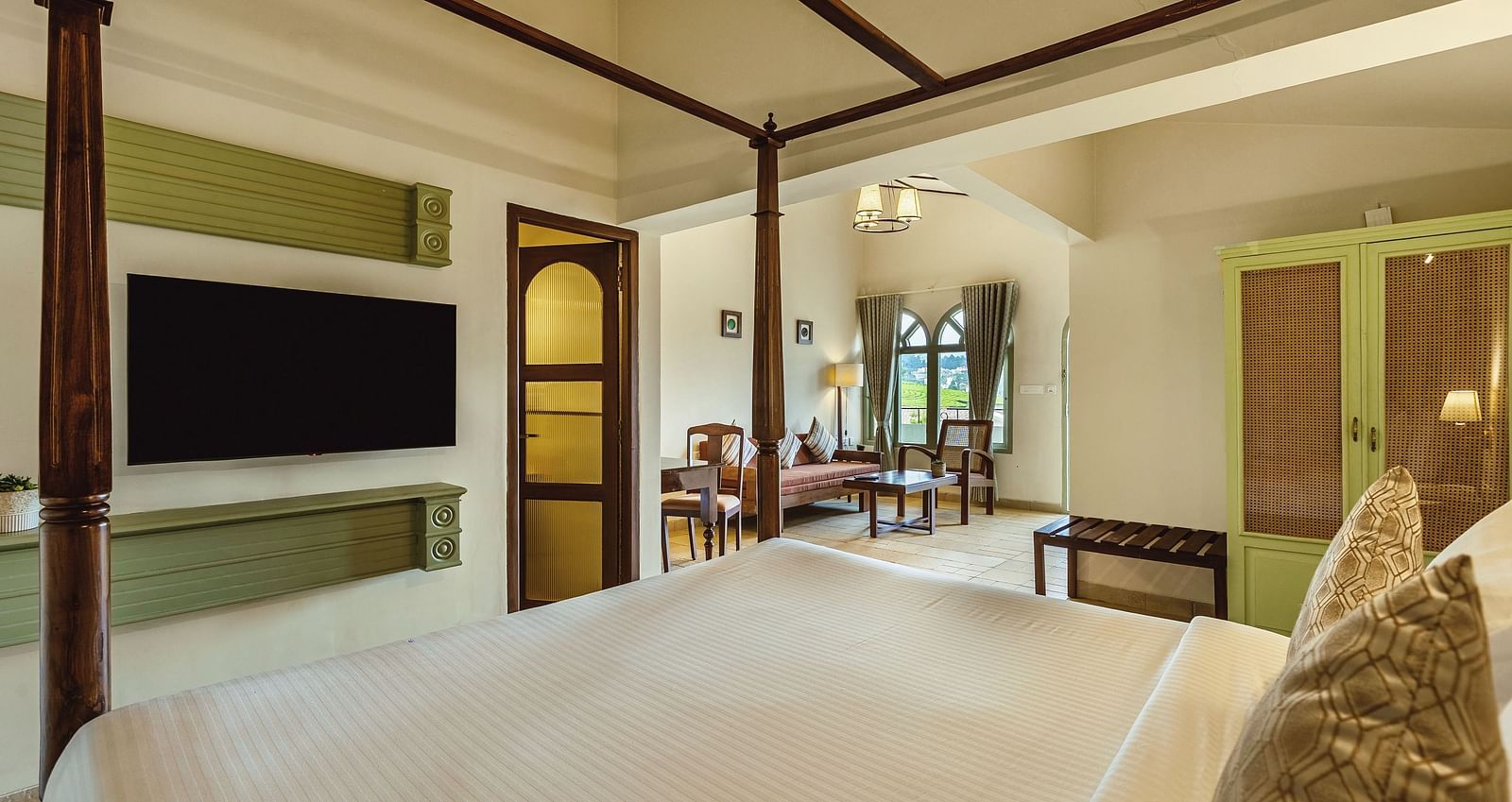 A four-poster bed in a well-lit bedroom at Mango Hill Shola, Ooty, with a large TV and tasteful interior design.