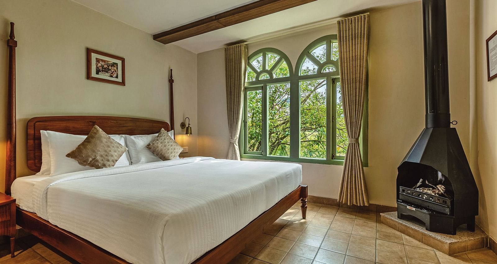 Junior Suite with Bathtub at Mango Hill Shola, Ooty with a canopy bed, fireplace, and large arched window framing scenic greenery.