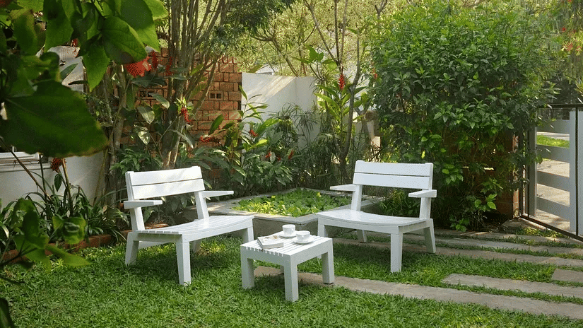 White garden seating set on a green lawn surrounded by trees and plants at Amanvana Spa Resort in Coorg.