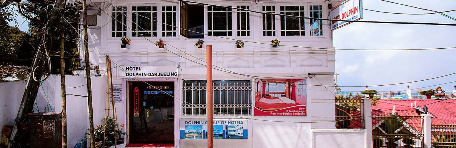 A 2-storey white guesthouse with a green railing and a light blue sky in the background at Hotel Dolphin Darjeeling.