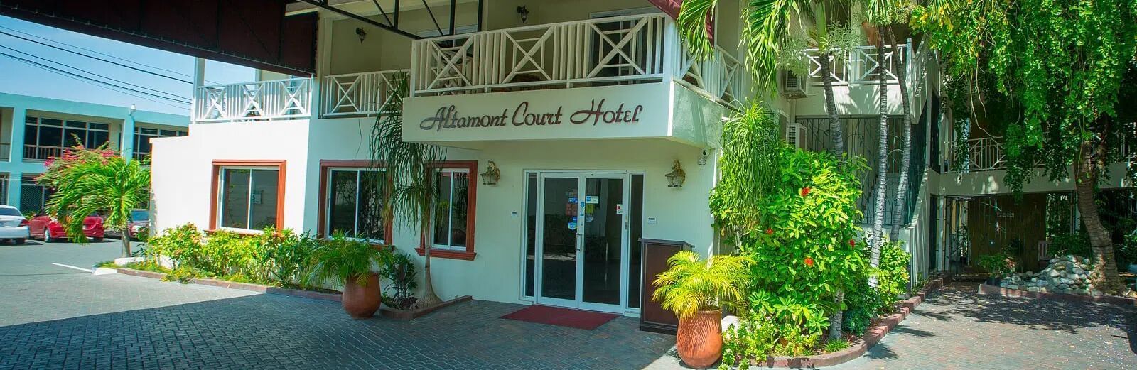 A low-angle shot of a white building with a covered entrance and lush green foliage | Altamont Court, Jamaica