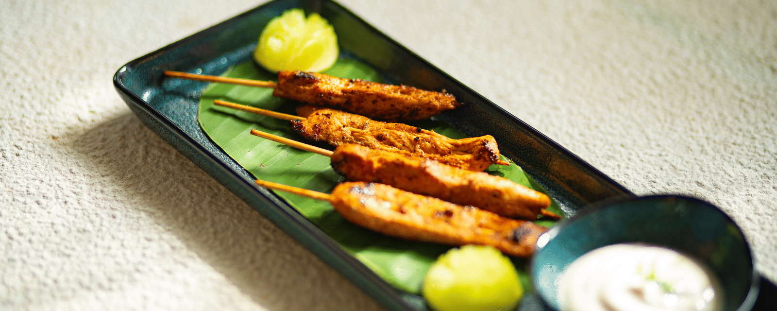 A plate of grilled chicken skewers with lime wedges and a side of sauce at Stanley Revelation.
