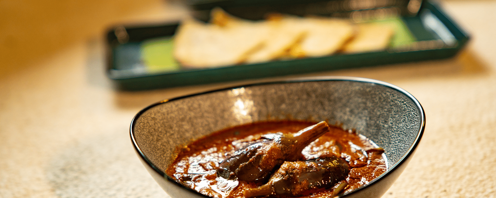 A bowl of rich, dark meat curry at Stanley Revelation, with other dishes blurred in the background.