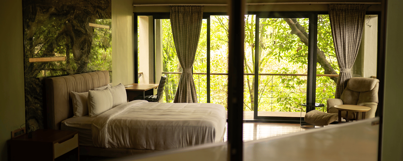 A bedroom at Stanley Revelation with a large bed, seating, and a balcony overlooking a forest.