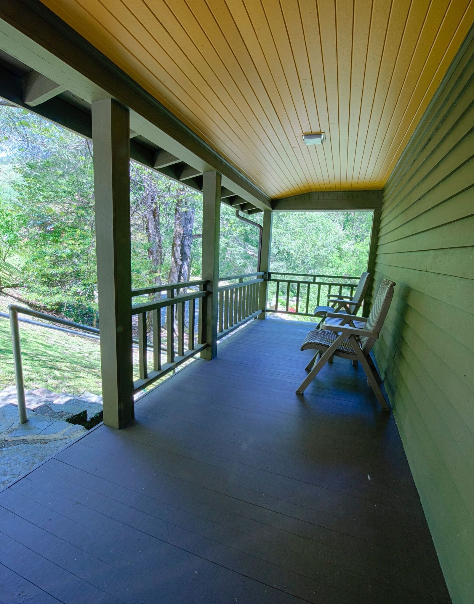 a wooden porch outside a cabin with two empty chairs overlooking the lush green surroundingsfull view image of a bedroom with wooden interiors featuring two beds - Historic Tapoco Lodge