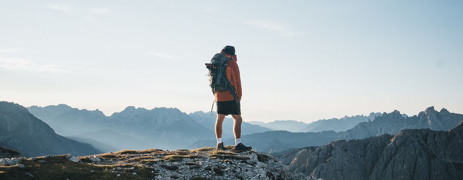 An image of a boy standing on a peak with a background of two hills and an open sky