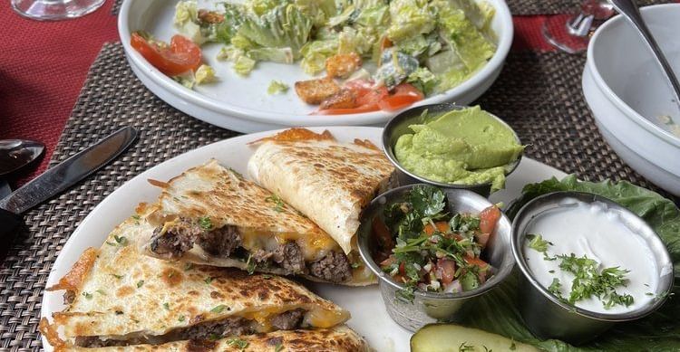 A table setting featuring a meal with a quesadilla, guacamole, salsa, and a side salad