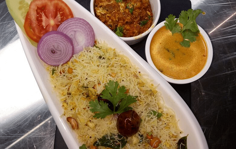  A white oval plate filled with yellow rice, garnished with cilantro. Accompanied by a small bowl of chutney and a half lemon.
