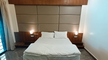 A close-up of a hotel room, focusing on a bed with a white duvet set against a wood-panelled headboard | Nandan Resort