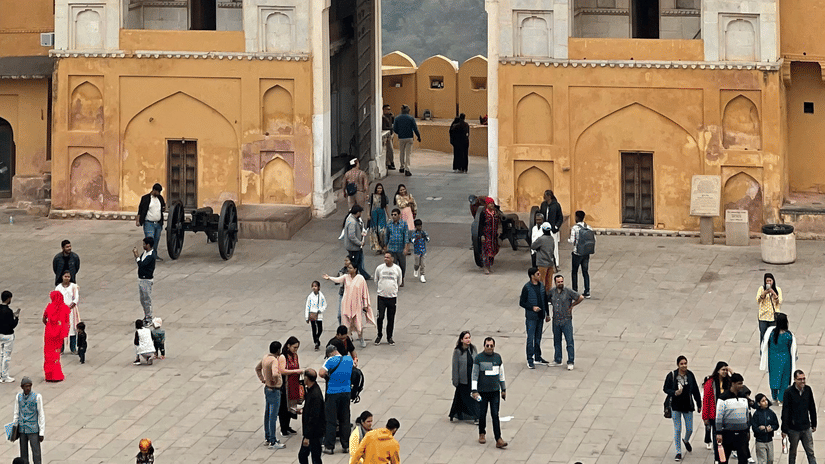 A large, ornate arched gateway stands at the entrance of a crowded courtyard, with a hill visible in the distance.