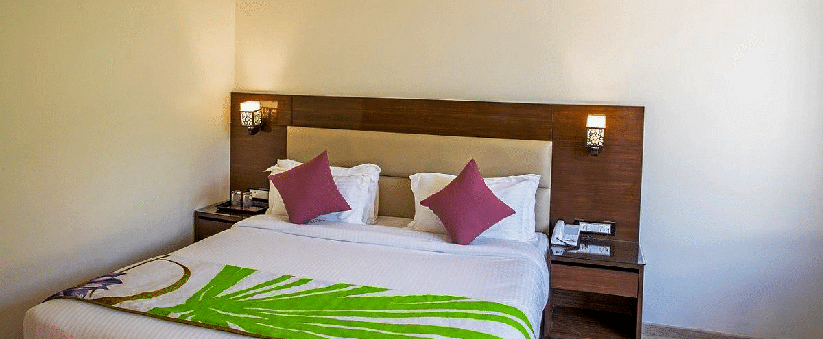 A close up shot of the double bed at the Premium Room at Regenta Inn DLS with two brightly lit lamps on either side of it.