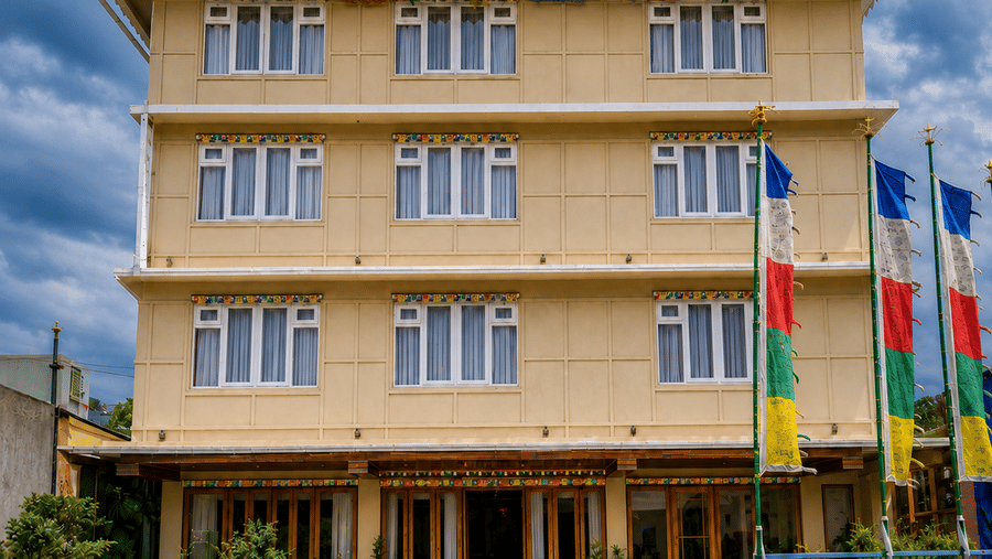 Daytime facade of Valmere Magnolia Boutique Hotel & Spa, Pelling, a 4-storey pale yellow building with Tibetan prayer flags and potted plants at the entrance.