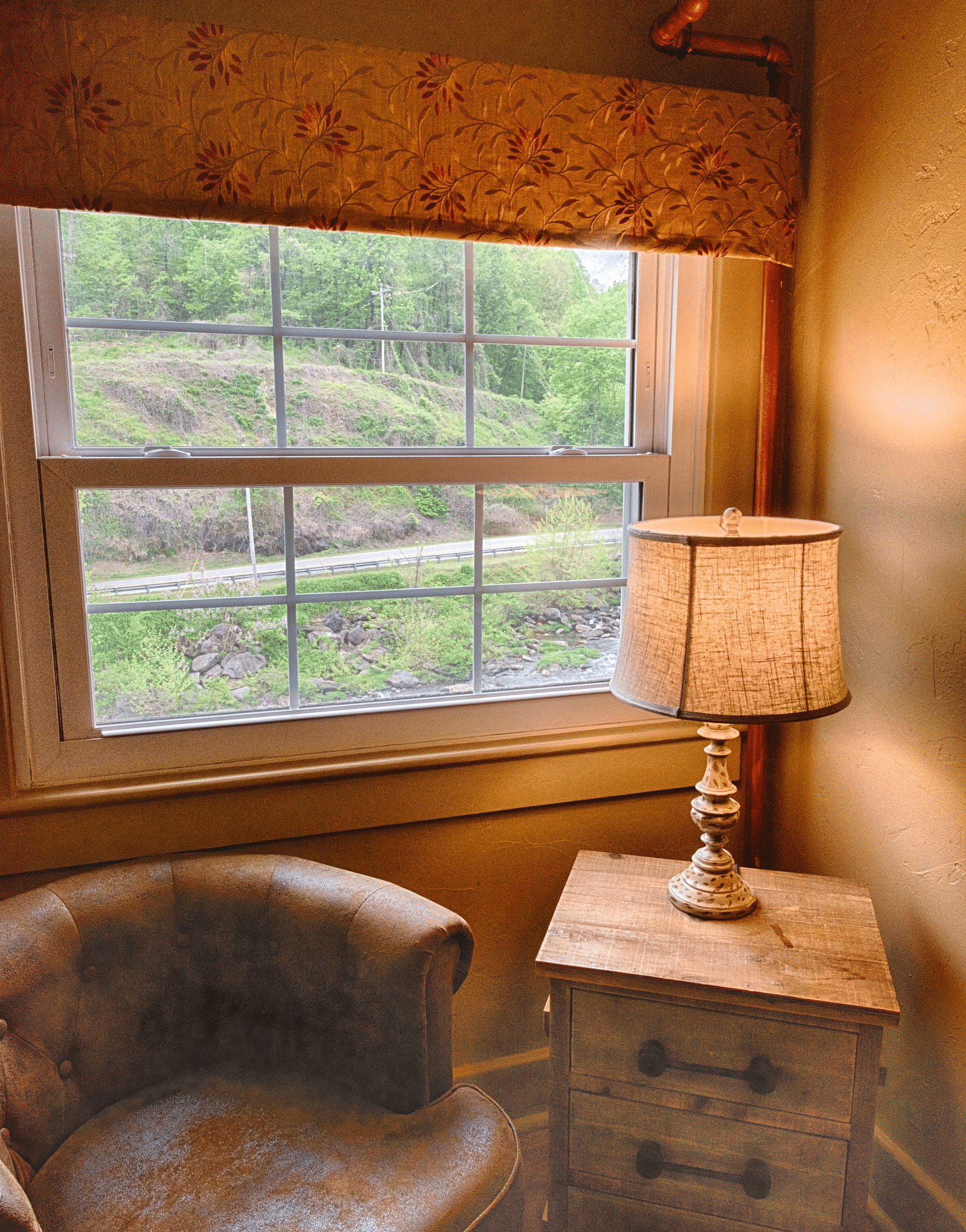 a close up image of a leather arm chair kept alongside a wooden table with a lamp over it - Historic Tapoco Lodge