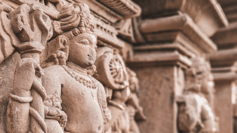 Close-up of intricately carved sandstone deity sculptures on the exterior wall of an ancient Indian Hindu temple showing detailed artistry.