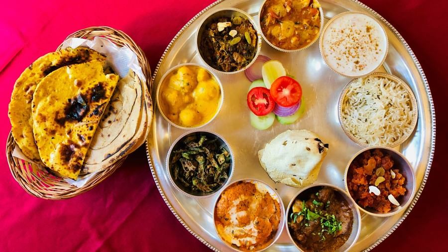 A highly appetising and vibrant North Indian Thali (platter) with many small bowls of curries, lentils, rice, and a side basket of Naan bread.