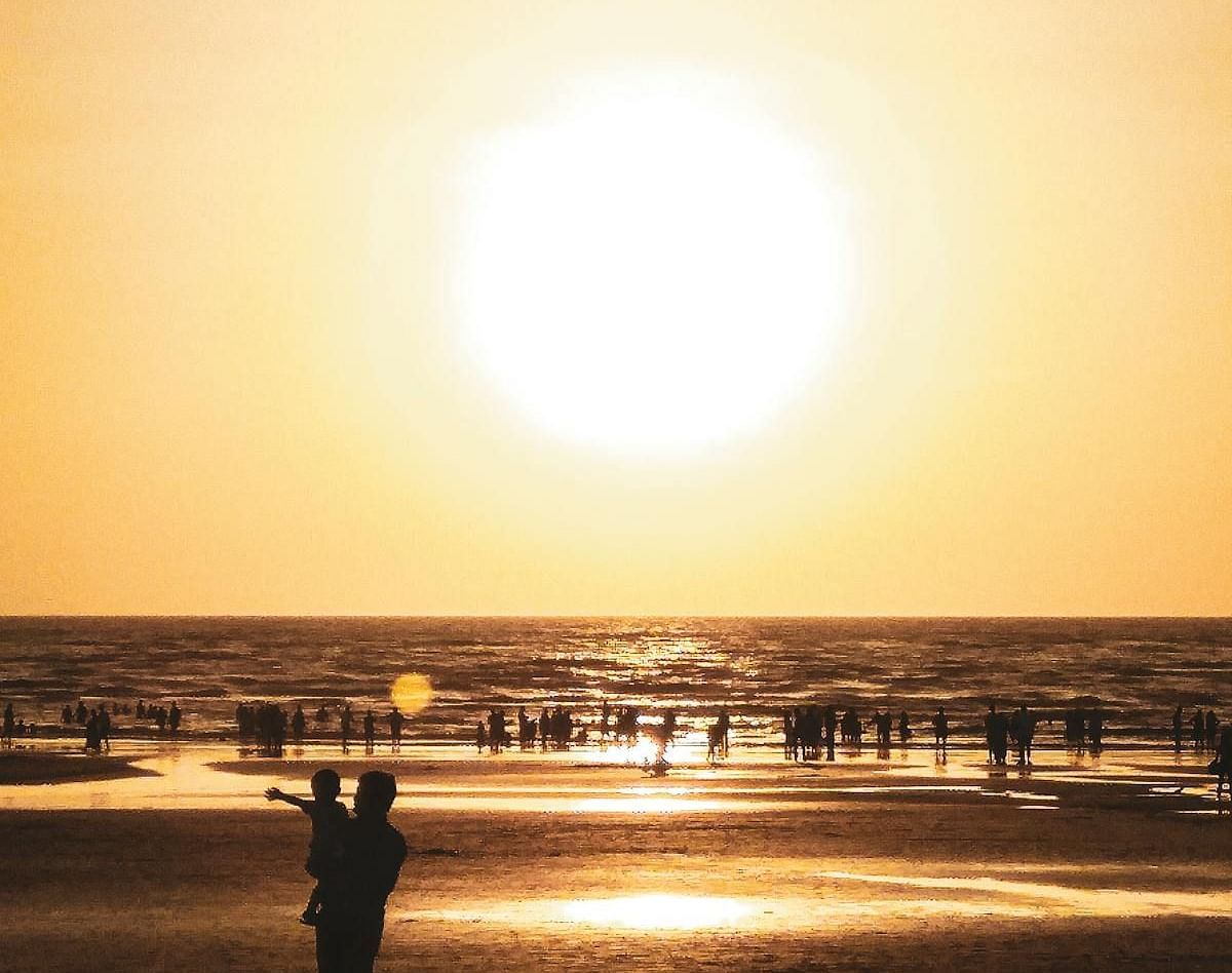 Bright celestial body above water and shore with indistinct shapes and a figure.