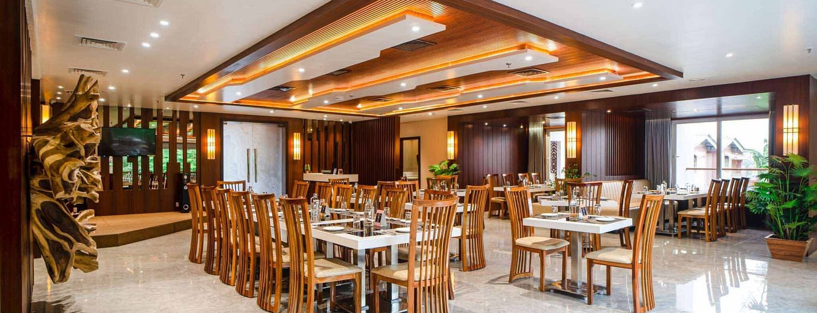 The spacious and brightly lit dining hall at Mansha Palace features numerous set tables and comfortable wooden chairs.