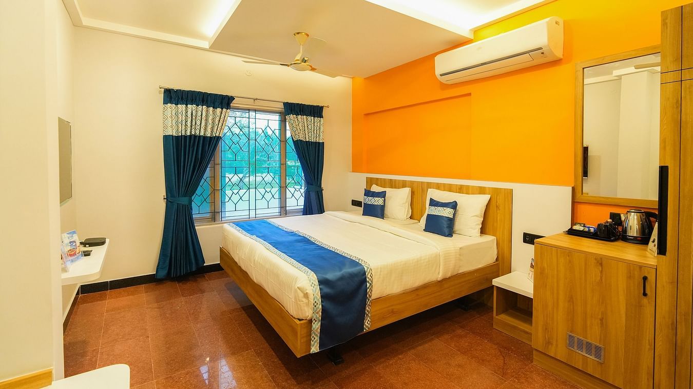 An image of a room with a bed, bed side table, a wall  mounted mirror, tea and coffee maker placed on a table, and a window overlooking the view - MGM Whispering Nest