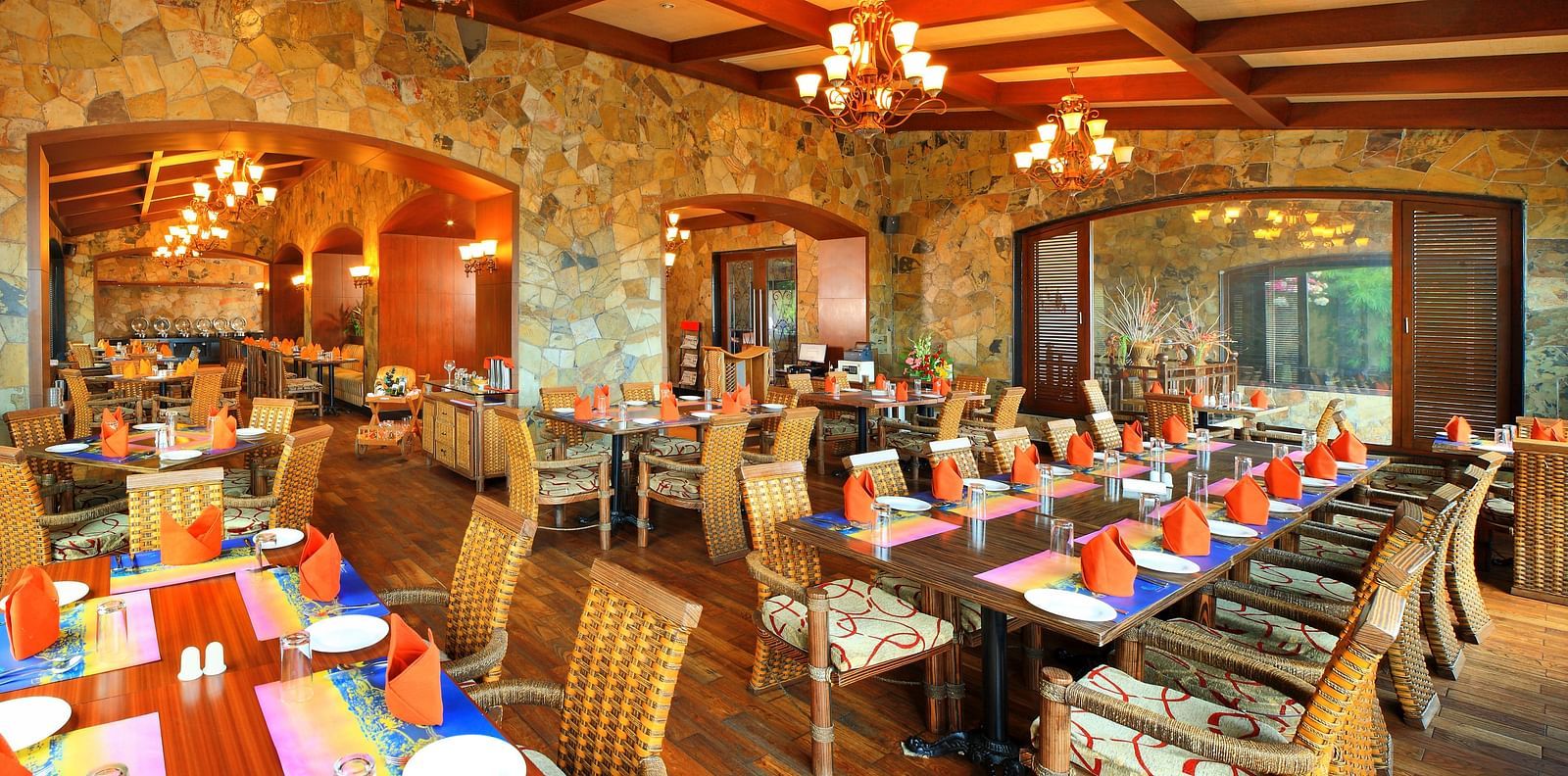 Amber restaurant at Ocean Spray Puducherry featuring wooden tables and chairs set, plates, cutlery, mat, and hand towels are placed on the table