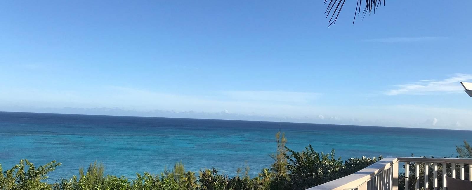 View of the ocean and trees from a deck with a chair and railing | A Stone's Throw Away