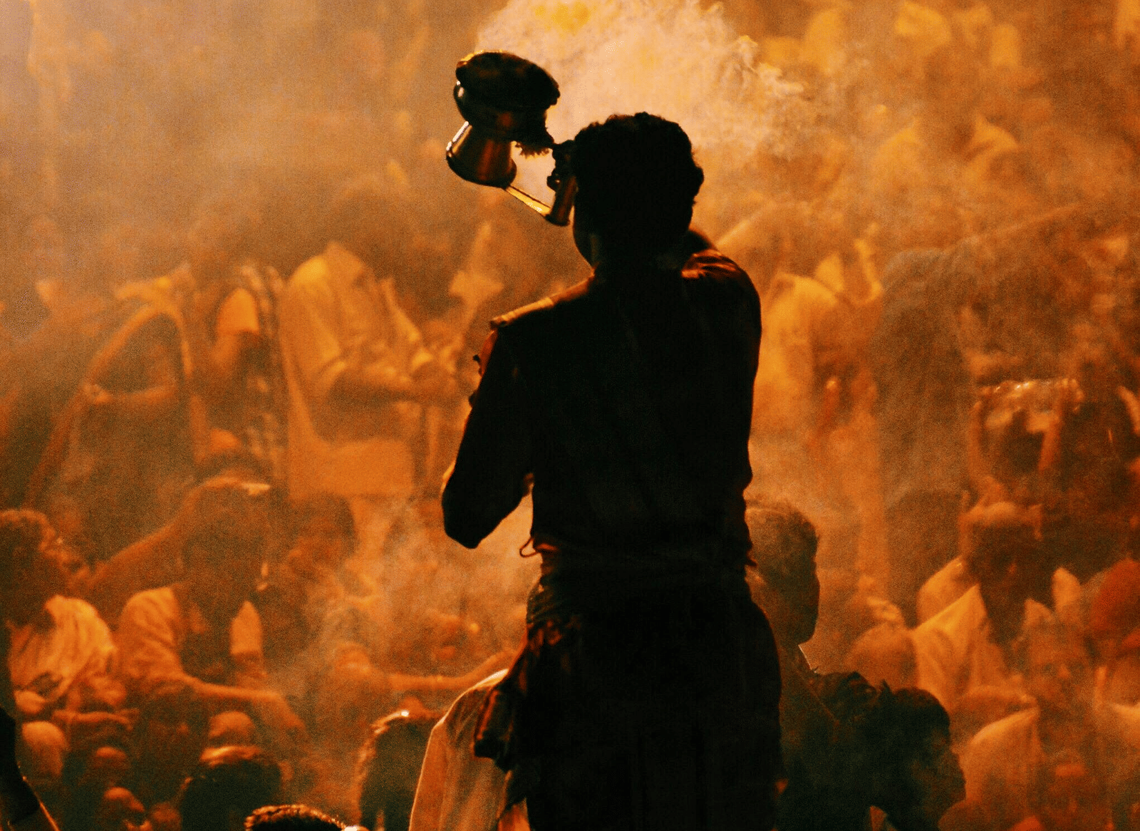 A silhouette of a priest performing aarti facing the crowd of devotees.