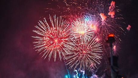 An overview of a lakeside venue with firecrackers in the sky that is illuminated on the waterbody