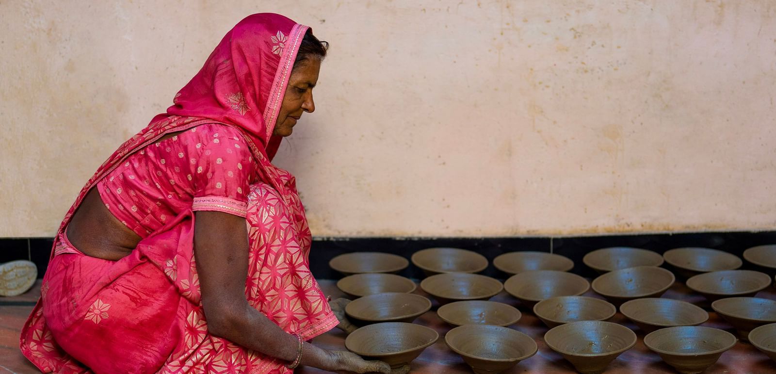 image of a woman draped in a pink saree lining up clay bowls on the floor