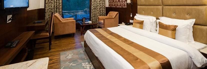  A spacious and well-lit hotel room featuring a comfortable bed, seating area, and a flat-screen TV | DLS La Serene Manali