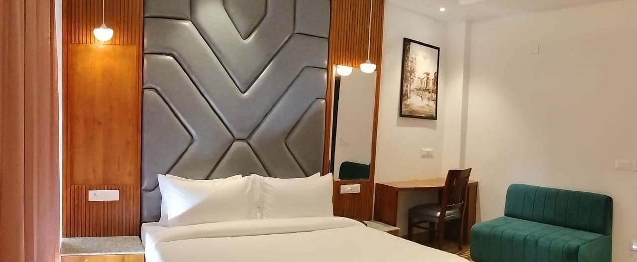 A large bed placed next to a sofa in Premium Room With Balcony at DLS Ark Holiday Inn, Banikhet.