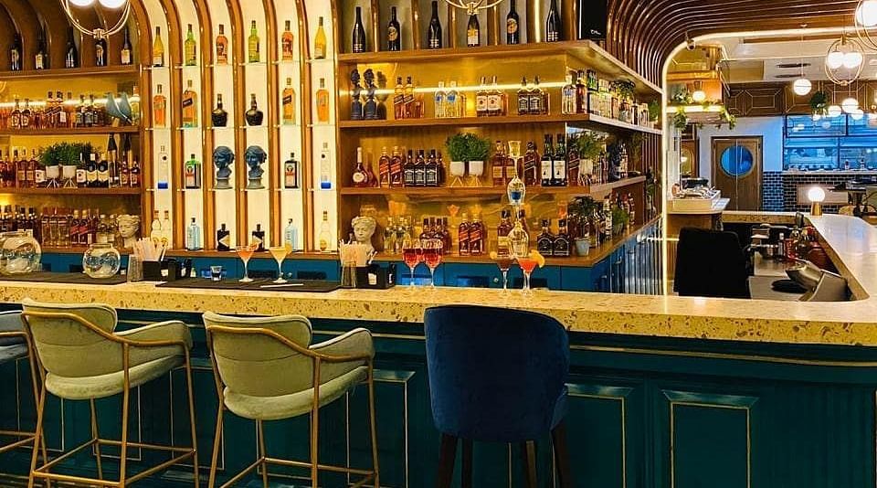 An image of a bar featuring a counter table, stools, and a shelf where liquor items are placed - Themis Barbecue House, Panipat