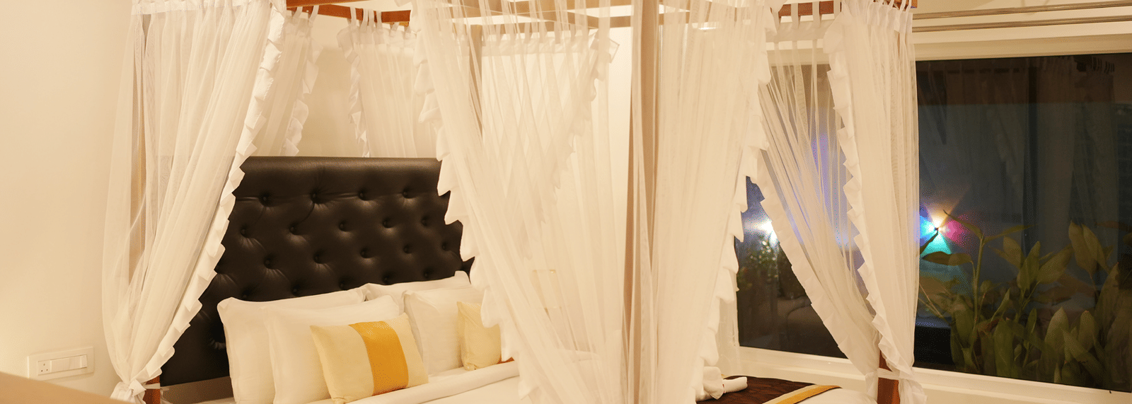 A modern bedroom featuring a four-poster canopy bed draped with white fabric and luxurious gold bedding at Coorg Orange Blossom Resort and Spa.