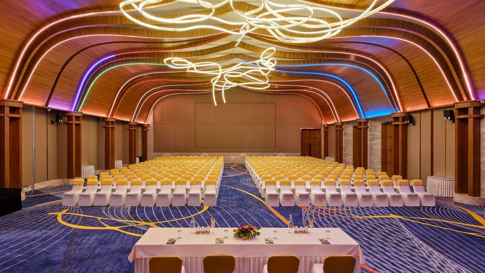 Image of the meeting hall Boito Voyage at Swosti Premium Beach Resorts in Puri featuring a large sitting area for audience under warm lighting and four chairs arranged with a large table facing the audience