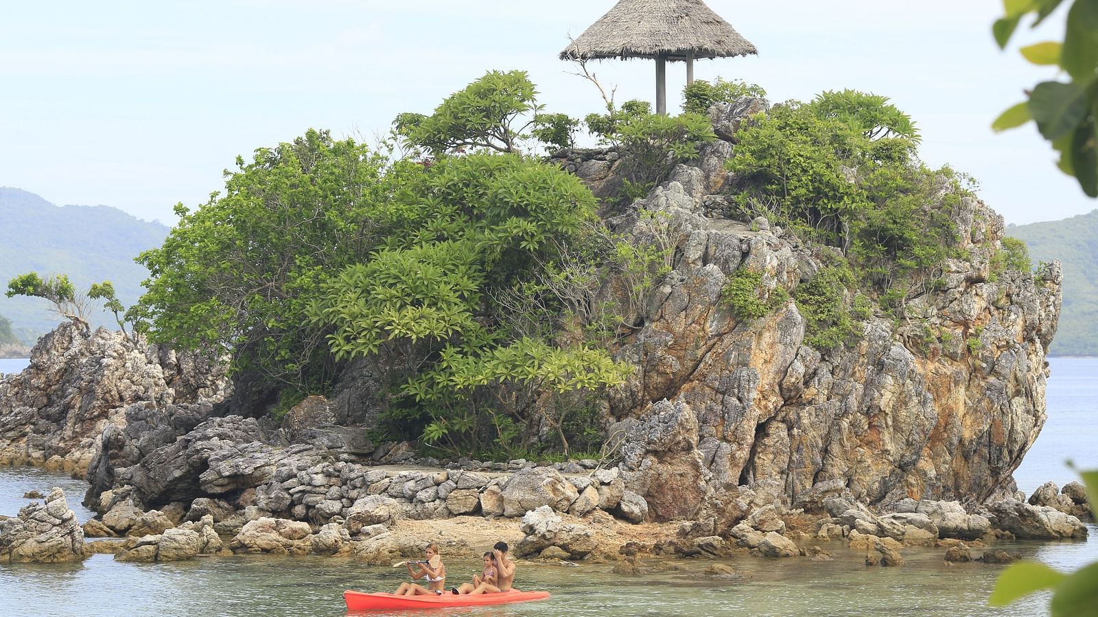  Small rocky island with a thatched hut and a kayak in the water at Flower Island Resort.