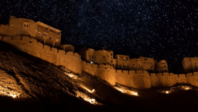 Jaisalmer Fort is illuminated at night with a starry night sky above, in Rajasthan, India.