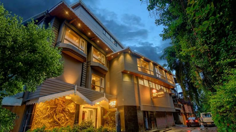 An image of a well lit facade surrounded by trees and there is also a driveway near the entrance - Sumi Yashshree Hotels & Resorts