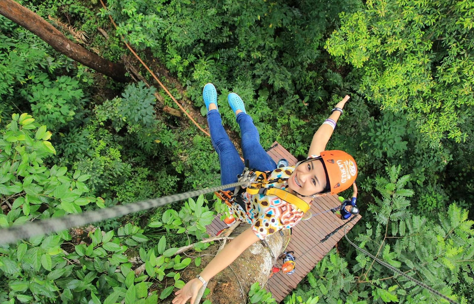 An image of a girl hanging from a cable with a backdrop of forest at the bottom
