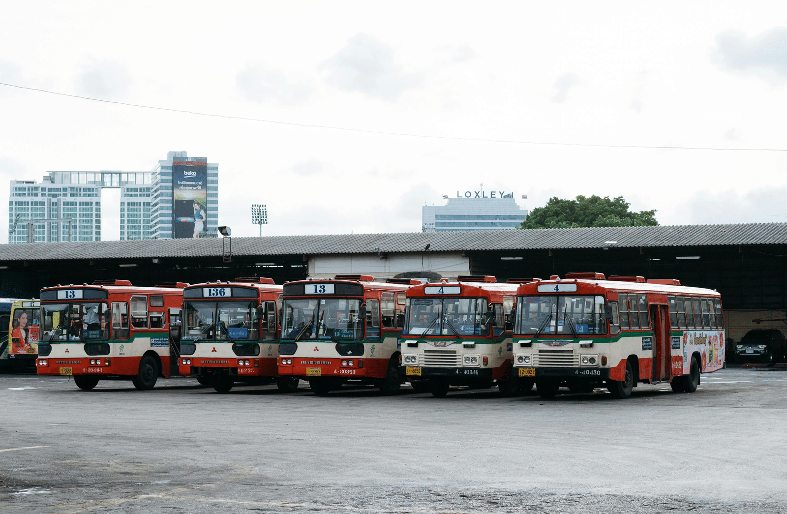A bus depot with five busses parked together closely.