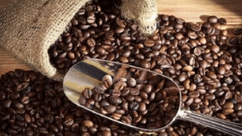Freshly roasted coffee beans spilling from a burlap sack with a metal scoop filled with coffee beans on a wooden surface.