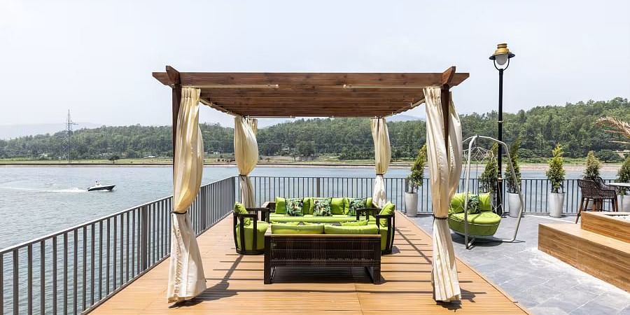 A wooden gazebo with a seating area overlooking a lake, with boats visible in the distance.