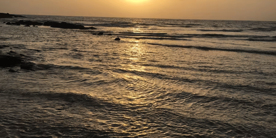 A sunset view over the sea with waves approaching the shore.