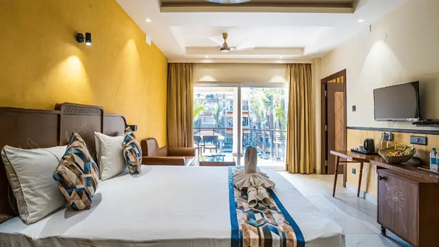 The bedroom in our Premium Suite featuring a large bed placed in front of a mounted television, a seating area, and a balcony | Hotel Sonar Bangla, Tarapith
