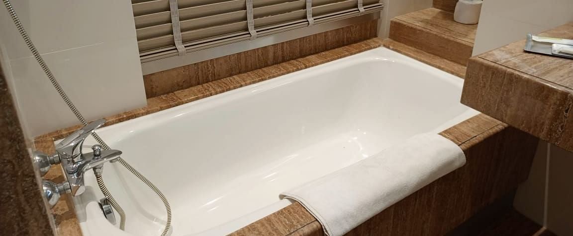 A modern bathroom in an executive room at Mirage Hotel, featuring a white, built-in bathtub, and a wall-mounted hand shower.