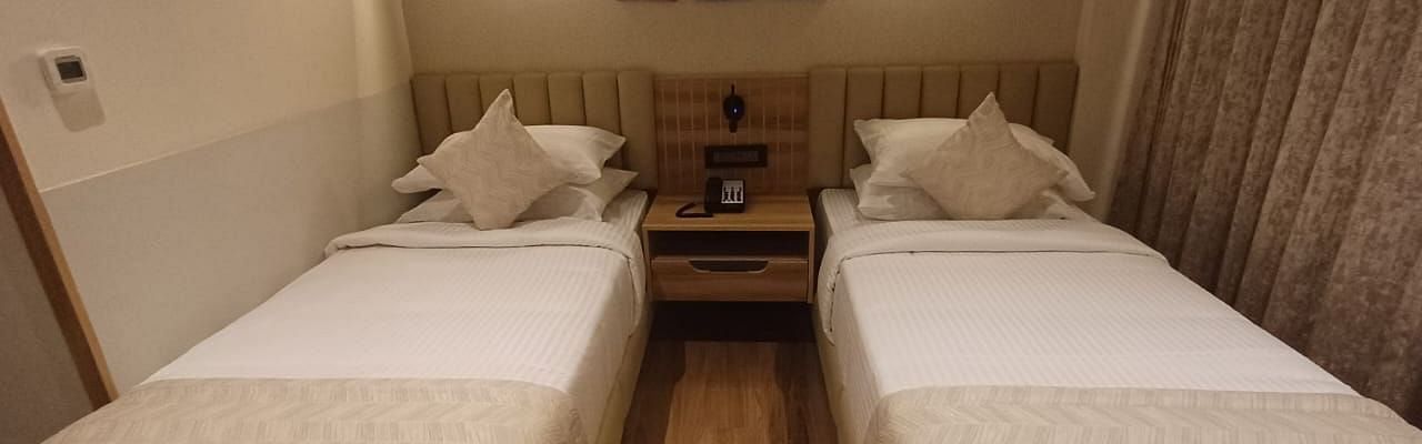 Image of a room with twin beds and a lights above the bed  at Hotel Raai, Hosur.