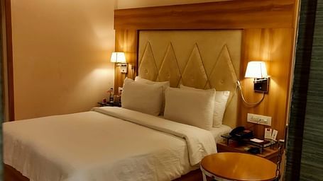 A cosy hotel bedroom  featuring a neatly made bed, bedside lamps, and a decorative headboard - Rang Lords Inn Bharuch